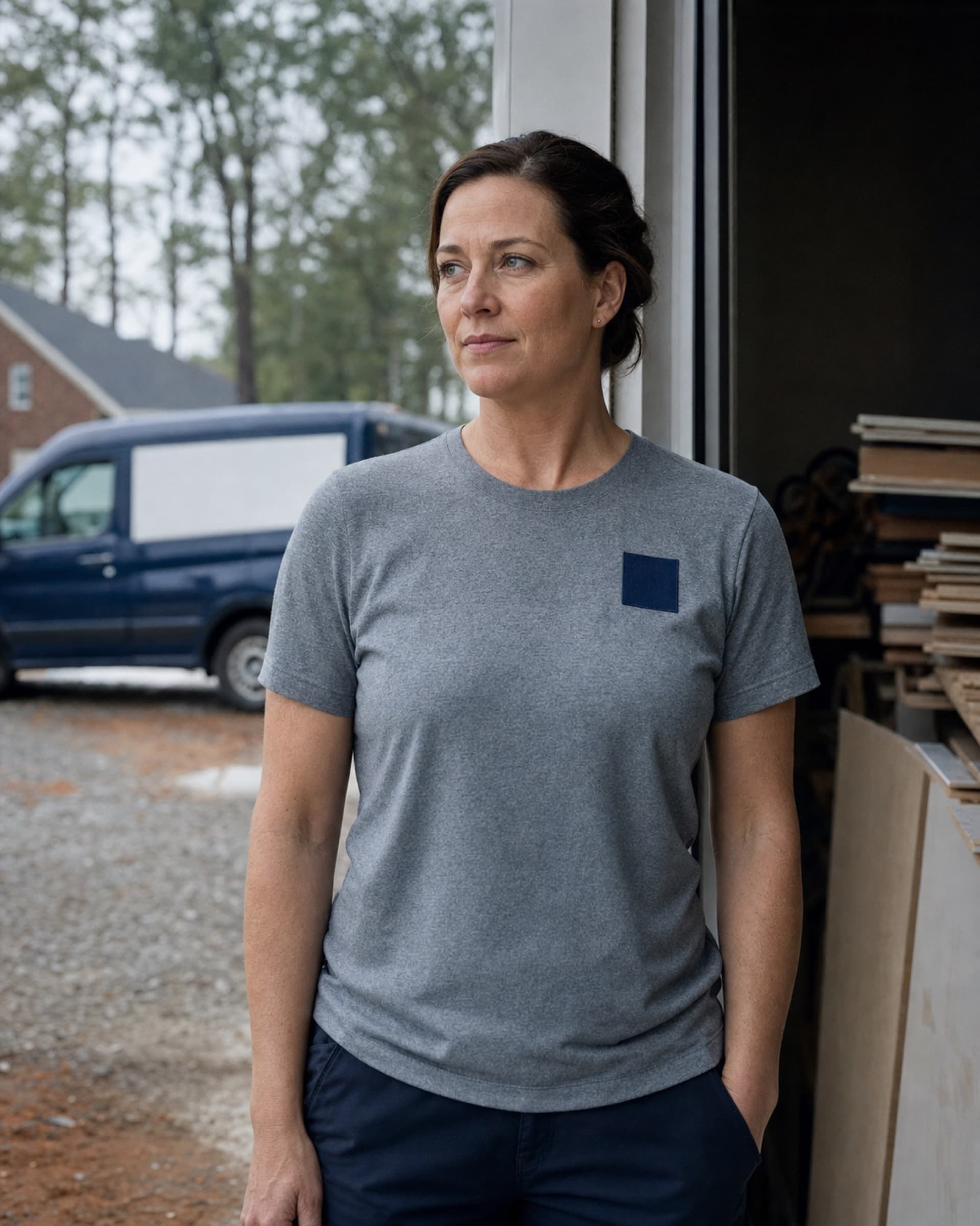 Lena Marchetti outside the yard office in a heather-grey work shirt, looking off camera